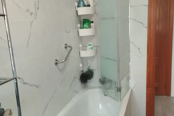 Reforma de baño en Málaga con alicatado de gran formato veteado aspecto mármol, plato de ducha y mampara plegable por REFORMAS A Plomo y Nivel
